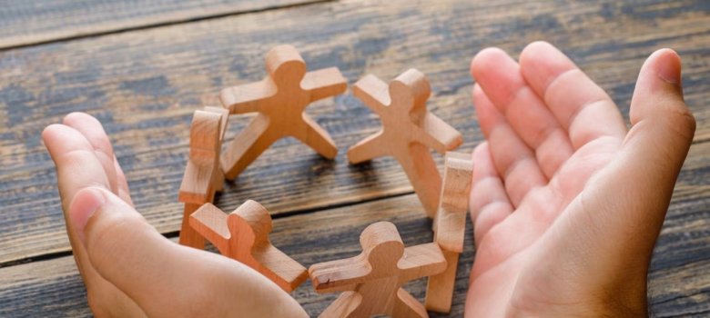 Kreis aus Holzfiguren zwischen zwei ausgefalteten Händen
